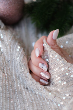 A beautiful oval-shaped Christmas manicure set against a glittery background. A winter trend featuring beige gel polish (Shellac). Space for text.