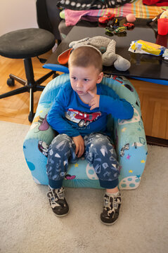 A curious boy in pajamas sits peacefully in his colorful chair, enjoying a quiet afternoon of indoor play