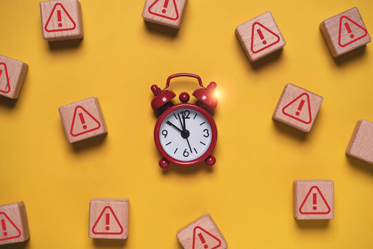 Urgent deadline and time pressure concept with red alarm clock surrounded by warning symbols on yellow background, representing risk, crisis, countdown, delay, urgency and time management.