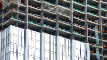 High rise building under construction with concrete framework and modern facade installation showing urban development process © belavinstock