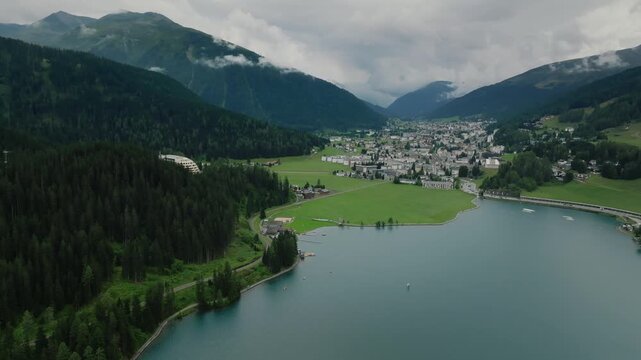 Aerial drone view of alpine lake town in mountain valley pine forests cloudy Switzerland