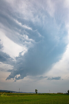 Dramatic rotating storm cloud and sweeping dark sky loom over a green open field.