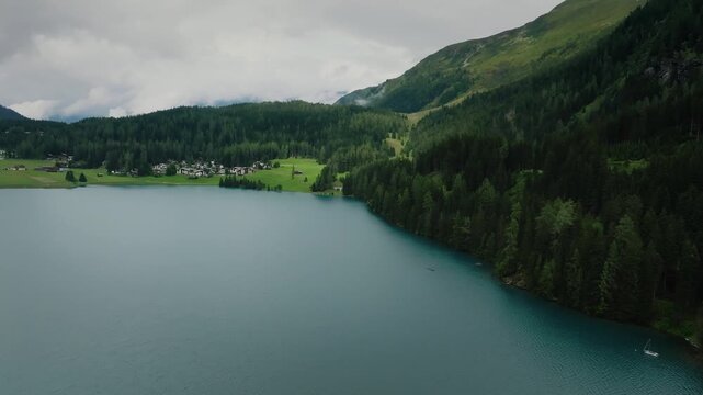 Aerial drone view of alpine lake town in mountain valley pine forests cloudy Switzerland