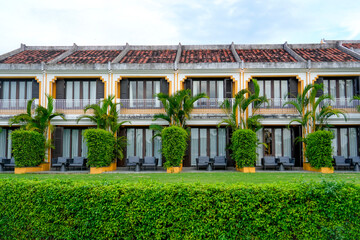 Fototapeta premium Bright facade of a traditional building in Vietnam displays charming balconies and neatly manicured shrubs during a serene afternoon retreat