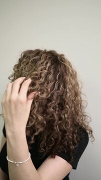 Woman gently fluffs and shapes her long natural curls with her hand, showing defined texture and volume after professional curly hair styling.