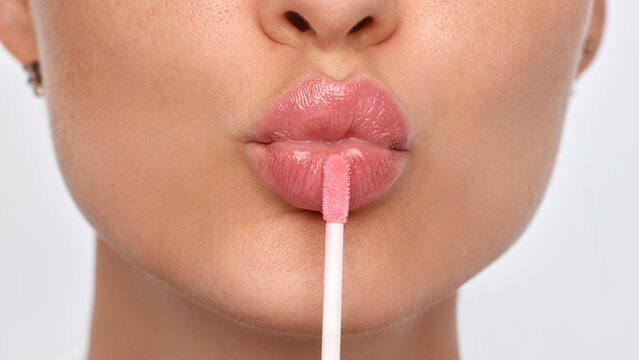 Gloss applicator touching puckered pink lips. Concept of lip care, cosmetic application, product advertising, beauty tutorials and daily skincare.