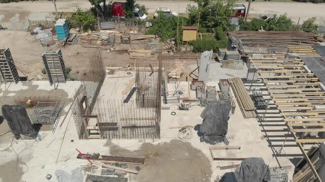Construction site aerial view showing concrete formwork, scaffolding, timber beams, and heavy equipment moving through busy work zone in daylight