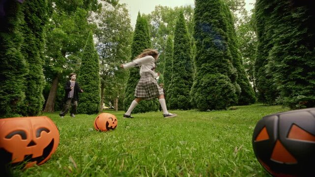 Multiethnic teenagers wearing Halloween costumes and zombie makeup running through hedge garden with pumpkin decorations. Useful for seasonal holiday advertising and youth festival promo campaigns