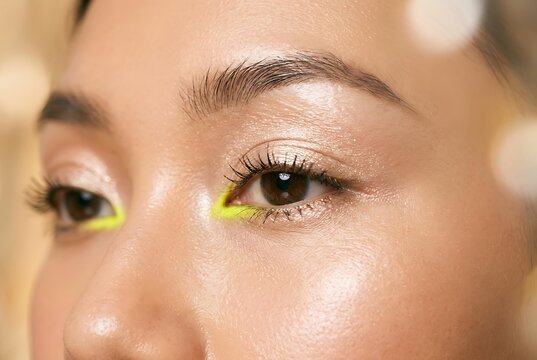 Close up of professional neon makeup on beautiful woman eyes, creative neon makeup style with yellow liner, fashion model with glowing skin and neon makeup for editorial look.