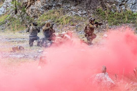 Military training exercise with smoke signals during a tactical maneuver in a rocky terrain