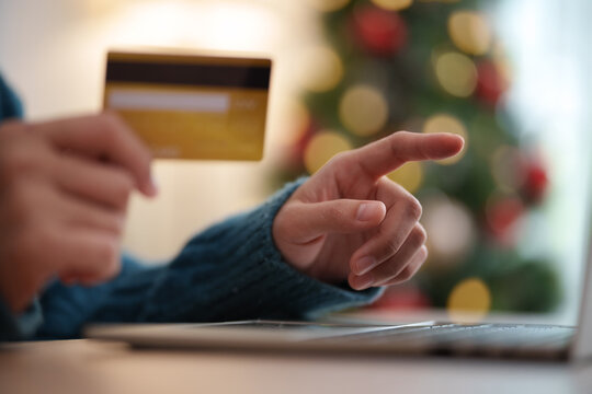 Person holding credit card and pointing toward a laptop during Christmas shopping, representing online purchase, digital payment, e-commerce checkout, holiday deals and cashless spending.