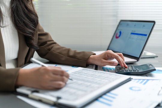 Businesswoman reviewing financial reports and using a calculator, representing accounting, finance analysis, budgeting, data review and planning.