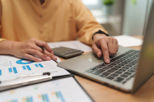 Professional analyzing financial reports and typing on a laptop beside a calculator and charts, representing accounting, budgeting, data analysis, business performance and financial planning.