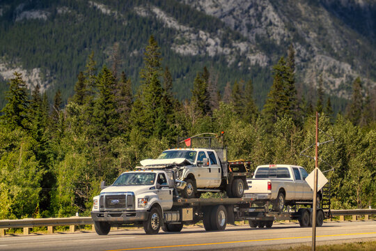 Canmore, AB, Canada - Sept 15, 2026: Heavy flatbed tow truck transporting damaged pickup trucks along a scenic mountain highway.