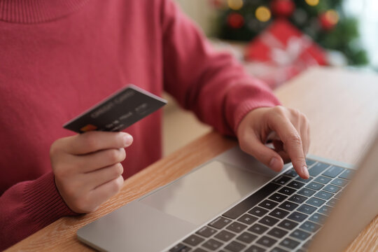 Woman holding credit card and typing on a laptop for online Christmas shopping, representing digital payment, e-commerce checkout, holiday purchases, cashless spending and seasonal sales.