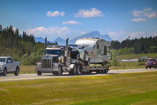 Canmore, AB, Canada - Sept 15, 2026: Heavy flatbed semi-truck transporting a pickup and fifth-wheel RV trailer along a mountain highway.