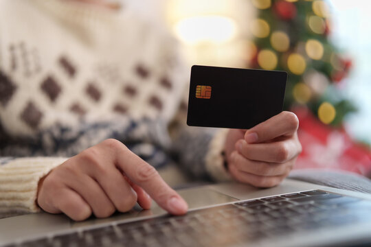 Person holding a credit card while shopping online on a laptop during Christmas, representing holiday purchases, digital payment, e-commerce checkout, seasonal spending and festive sales.