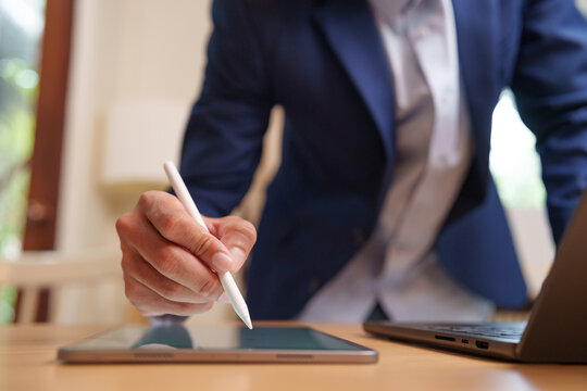Businessman using a stylus on a digital tablet beside a laptop, representing digital work, business productivity, technology, planning, workflow and modern workplace.