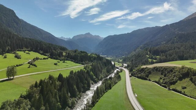 Aerial drone view of a mountain road and river running through a green alpine valley in Switzerland