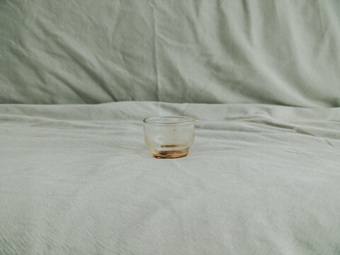 Small clear glass with brown residue on a wrinkled light fabric surface