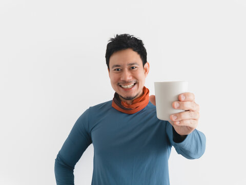 Cheerful Asian man in blue shirt holding a white cup, smiling at the viewer.