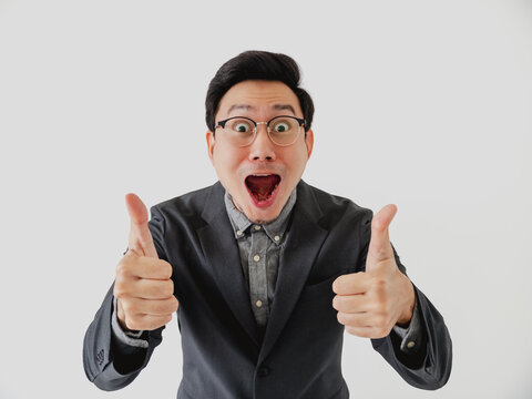 A cheerful Asian man in a suit and glasses expresses approval with two thumbs up.