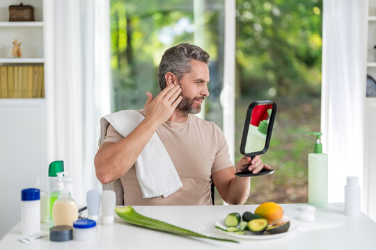 Mature man look at mirror on his perfect skin. Anti-aging and wrinkle concept. Man touch face at mirror. Skincare and male beauty. Check skin after using anti aging beauty product