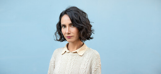 Woman with short wavy bob hairstyle stands against a blue background during the day © nikopacheco