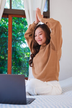 Vertical portrait of a woman meditating or practicing yoga on bed in front of laptop computer
