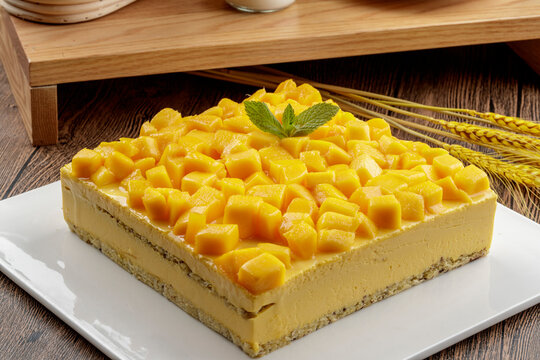 A three-tiered mango cream cake is placed on a wood-grain base.