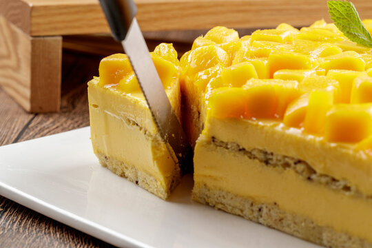 A three-tiered mango cream cake is placed on a wood-grain base.