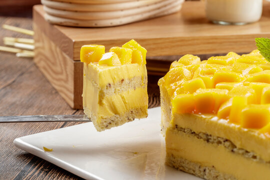 A three-tiered mango cream cake is placed on a wood-grain base.