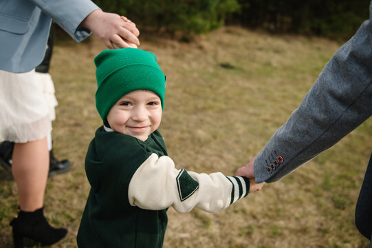 Cute little boy holding hands with parents outdoors during a spring family walk in the park. Close-up portrait.
