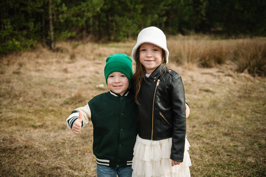 Cute little boy showing thumbs up while posing with a girl outdoors in a pine forest during a seasonal family photo session.