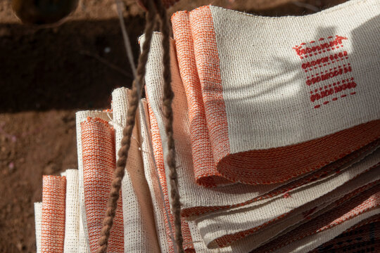 Folded Senufo cotton cloths with orange stripes and embroidered patterns catch the sunlight at a street market, Savanes district, Waraniene, Ivory Coast