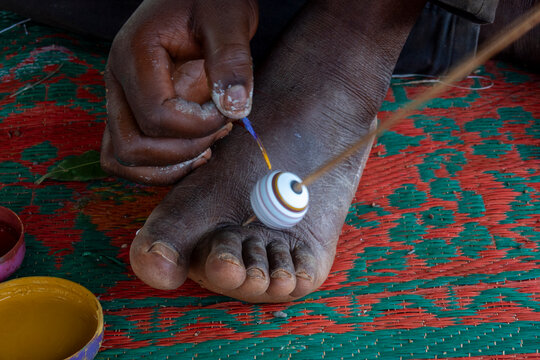 A Senufo craftsman paints colorful stripes onto a clay bead held steady with his foot, Savanes district, Waraniene, Ivory Coast