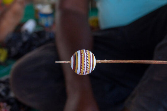 A Senufo craftsman's hand-painted clay bead with striped patterns rests on a wooden stick, Savanes district, Waraniene, Ivory Coast
