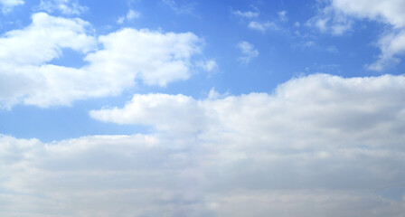 Fototapeta premium Fluffy white clouds drift across a clear blue sky during a bright sunny day with gentle sunlight