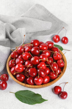 Fresh ripe sweet cherries in rustic wooden bowl with green leaves and linen cloth on white textured background. Healthy summer fruit, red berries, fresh seasonal harvest, healthy food