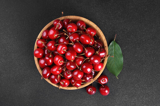 Fresh ripe sweet cherries in rustic wooden bowl on black stone textured background with copy space for text. Juicy organic summer fruit, red berries, healthy seasonal food, farm harvest