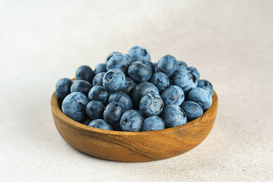 Fresh ripe blueberries in wooden bowl on a light gray textured background. Seasonal summer harvest, healthy food, natural nutrition, wholesome eating and nutritious source of vitamins and antioxidants