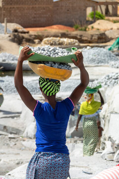 A woman lifts a basin of crushed granite onto her head at the quarry as others work behind her, Savanes district, Shienlow, Ivory Coast