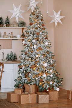 Fully decorated Christmas tree with golden and white ornaments and presents, wrapped gift boxes. Cozy festive interior perfect for winter holiday themes and seasonal projects.