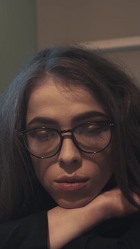 Sad woman in glasses resting chin on folded arms, emotional exhaustion and loneliness. Postpartum depression and maternal mental health awareness. Vertical video.