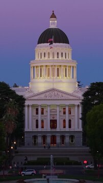 Aerial view highlights the California State Capitol in Sacramento during the evening with surrounding trees and lights visible.