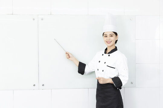 Smiling Female Chef in Uniform Pointing at Blank Whiteboard