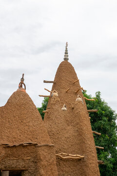 Wooden support pegs jut from two mud towers of the 17th-century Sudano-Sahelian mosque beside a mango tree, Savanes district, Kouto, Ivory Coast