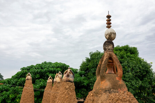 Ceramic-capped pinnacles cluster beneath a crescent finial half-hidden by leaves at the 17th-century Sudano-Sahelian mosque, Savanes district, Kouto, Ivory Coast