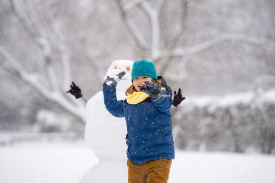 Child throw snowball, winter happiness. Child throwing snow near a snowman. Child in warm clothes play with snow during winter. Child smiling in snowball fight . Winter childhood.
