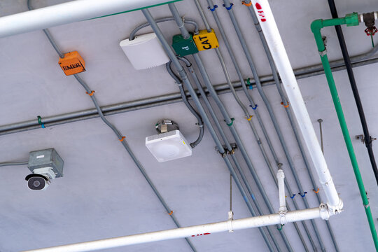 CCTV security camera and electrical conduit installed on building ceiling, infrastructure for video surveillance, electrical wiring, facility safety and security monitoring in a modern property.